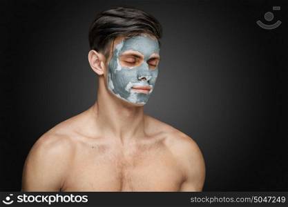 Portrait of a beautiful young man with a facial clay mask, face and body skin care treatment.