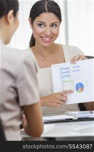Portrait of a beautiful young mixed race Hispanic woman or businesswoman in office meeting with female colleague using a graph of figures or statistics