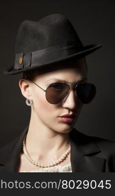 Portrait of a beautiful young model in black hat with sunglasses on black background