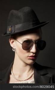 Portrait of a beautiful young model in black hat with sunglasses on black background