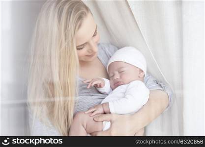 Portrait of a beautiful young mother holding her little precious baby, enjoying parenthood at home, child care and family love concept