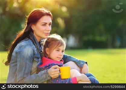 Portrait of a beautiful young mother with cute little daughter relaxing outdoors, drinking tea in the morning, with pleasure spending time together in the countryside, happy family life