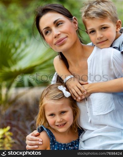 Portrait of a beautiful young mother with her two cute kids having fun outdoors, happy family with pleasure spending time together, enjoying summer holidays