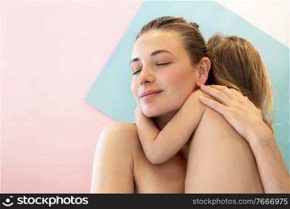 Portrait of a beautiful young mother with pleasure hugging her baby son, family photoshoot over pastel colorful background, family love and happiness concept