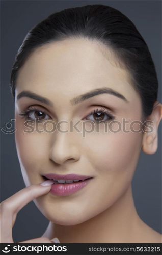 Portrait of a beautiful young woman biting fingernail over colored background