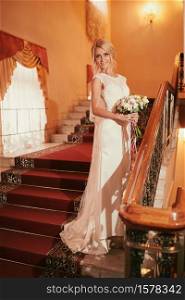 portrait of a beautiful young woman bride in a white dress with a bouquet of flowers in her hands on stairs indoors. wedding day.. portrait of a beautiful young woman bride in a white dress with a bouquet of flowers in her hands on stairs indoors. wedding day