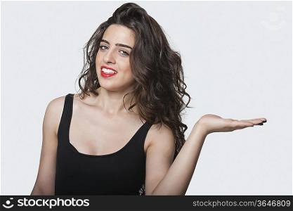 Portrait of a beautiful young woman holding her palm out over gray background