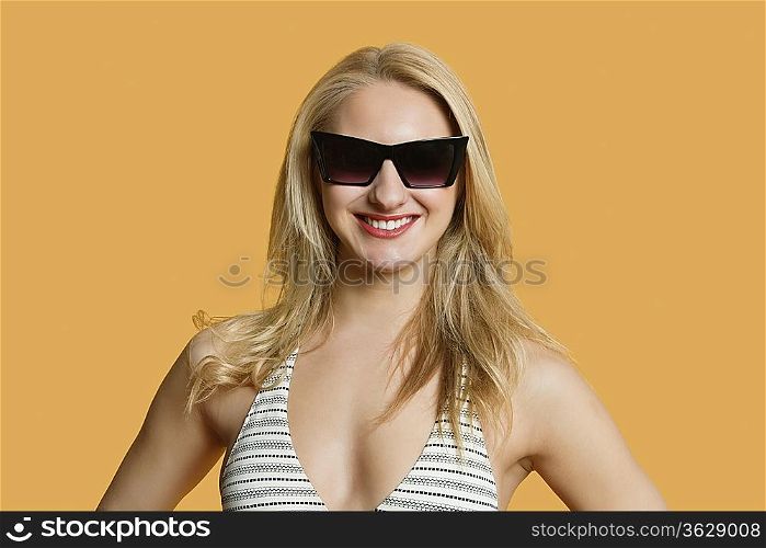 Portrait of a beautiful young woman in bikini wearing sunglasses over colored background