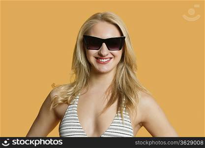Portrait of a beautiful young woman in bikini wearing sunglasses over colored background