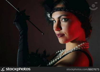 Portrait of a beautiful young woman in style of the great Gatsby of the 20s. Vintage clothing and jewelry. Portrait of beautiful woman smokes the mouthpiece. 20’s years.
