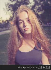 Portrait of a beautiful young woman in the city park. Outddors shot in the evening time. Toned Image.Romantic girl, attractive 20s blond female enjoying autumn yellow sunlight