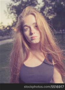 Portrait of a beautiful young woman in the city park. Outddors shot in the evening time. Toned Image.Romantic girl, attractive 20s blond female enjoying autumn yellow sunlight