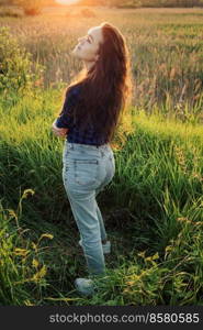Portrait of a beautiful young woman on meadow watching the sunset enjoying nature summer evening outdoors.