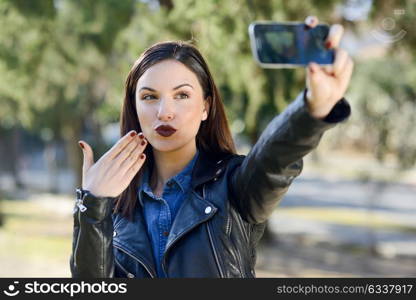 Portrait of a beautiful young woman selfie in the park with a smart phone. Girl blowing a kiss.