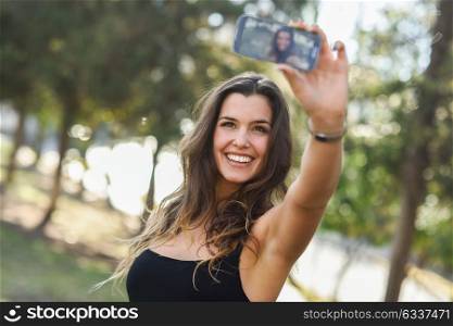 Portrait of a beautiful young woman selfie in the park with a smartphone