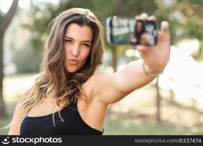 Portrait of a beautiful young woman selfie in the park with a smartphone