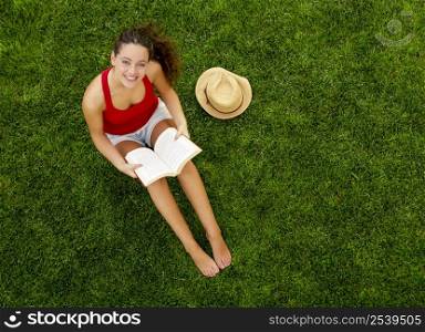 Portrait of a beautiful young woman sitting on the grass reading a book