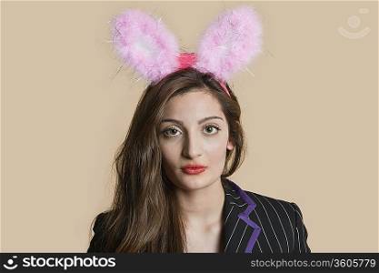 Portrait of a beautiful young woman wearing bunny ears over colored background