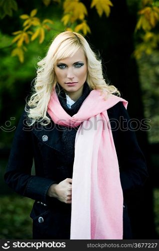portrait of a beautiful young woman with a black coat and a pink scarf in a fall outdoor park