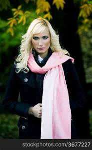 portrait of a beautiful young woman with a black coat and a pink scarf in a fall outdoor park