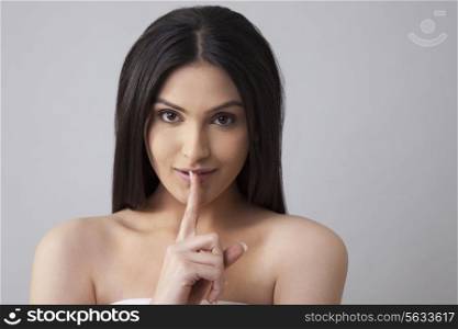 Portrait of a beautiful young woman with finger on lips over colored background