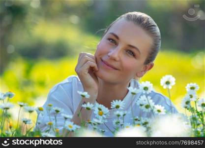 Portrait of a beautiful young woman with pleasure spending time outdoors, enjoying fresh daisy flowers on the floral meadow, happy spring holidays in countryside