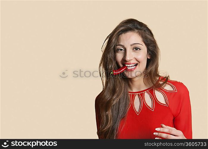 Portrait of a beautiful young woman with red chili pepper in mouth over colored background
