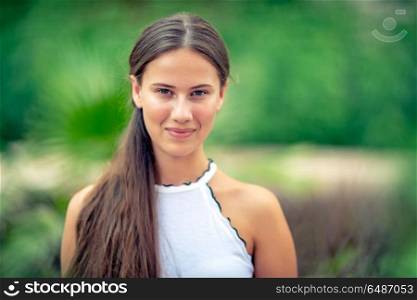 Portrait of a beautiful young woman without makeup standing over green park background, genuine beauty of youth, happy healthy lifestyle concept. Beautiful girl portrait