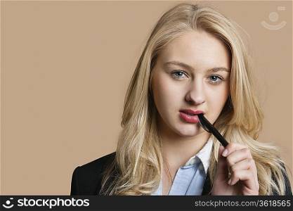 Portrait of a blond business woman with pen in mouth over colored background
