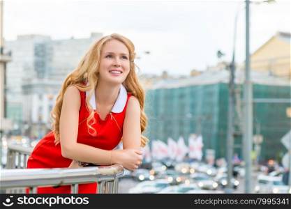 Portrait of a blonde leaning on the balcony railing against the backdrop of the city