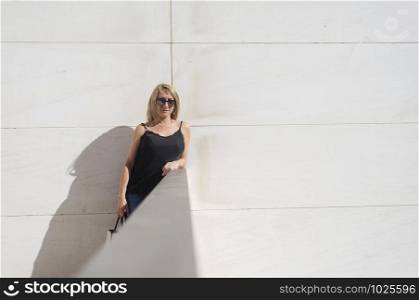Portrait of a blonde woman leaning on a white wall while looking camera