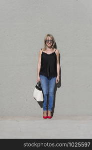 Portrait of a blonde woman leaning on a white wall while looking camera