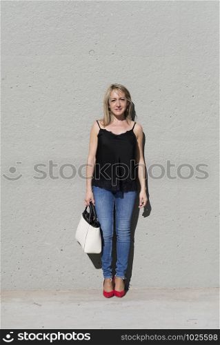 Portrait of a blonde woman leaning on a white wall while looking camera