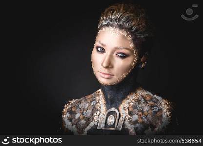 Portrait of a blue eyed young girl with creative golden makeup in the style of icon painting isolated on black background. Portrait a girl with Golden icon painting makeup