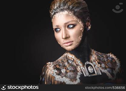 Portrait of a blue eyed young girl with creative golden makeup in the style of icon painting isolated on black background. Portrait a girl with Golden icon painting makeup