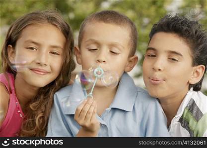 Portrait of a boy blowing bubbles with his sister and brother