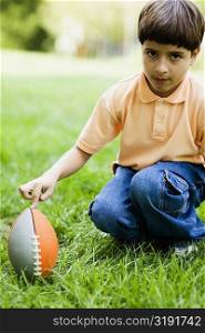 Portrait of a boy crouching with his finger on a rugby ball