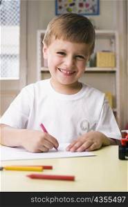 Portrait of a boy drawing on a sheet of paper and smiling
