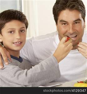 Portrait of a boy feeding his father a strawberry
