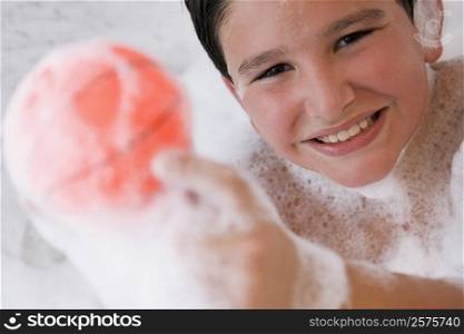 Portrait of a boy holding a ball in a bathtub and smiling