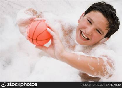 Portrait of a boy holding a ball in a bathtub and smiling