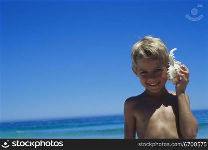 Portrait of a boy holding a conch shell against his ear