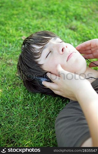 Portrait of a boy listening to music with headphones laid on the grass