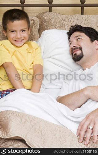 Portrait of a boy sitting on the bed with his father looking at him