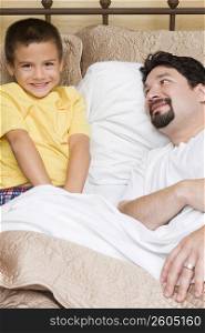 Portrait of a boy sitting on the bed with his father looking at him