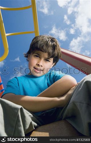 Portrait of a boy sitting with his arms crossed on a jungle gym
