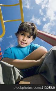 Portrait of a boy sitting with his arms crossed on a jungle gym