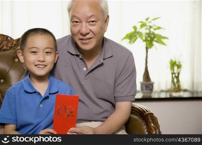 Portrait of a boy sitting with his grandfather and holding a red gift envelope
