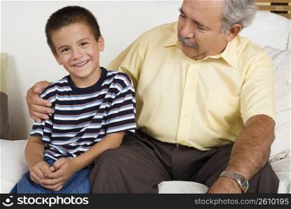 Portrait of a boy sitting with his grandfather on a couch and smiling