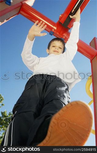 Portrait of a boy smiling and standing on a jungle gym with his hand raised